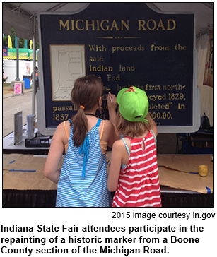 Two girls at the 2015 Indiana State Fair paint a Michigan Road historic marker from Boone County.