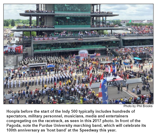Hoopla before the start of the Indy 500 typically includes hundreds of spectators, military personnel, musicians, media and entertainers congregating on the racetrack, as seen in this 2017 photo. In front of the Pagoda, note the Purdue University marching band, which will celebrate its 100th anniversary as 'host band' at the Speedway this year. Photo by Phil Brooks